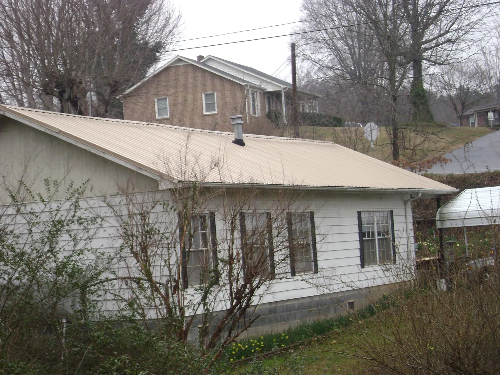 Tan metal roof on a white sided house set into a hillside — Commercial Roofing by Roofing Brothers in Hurricane